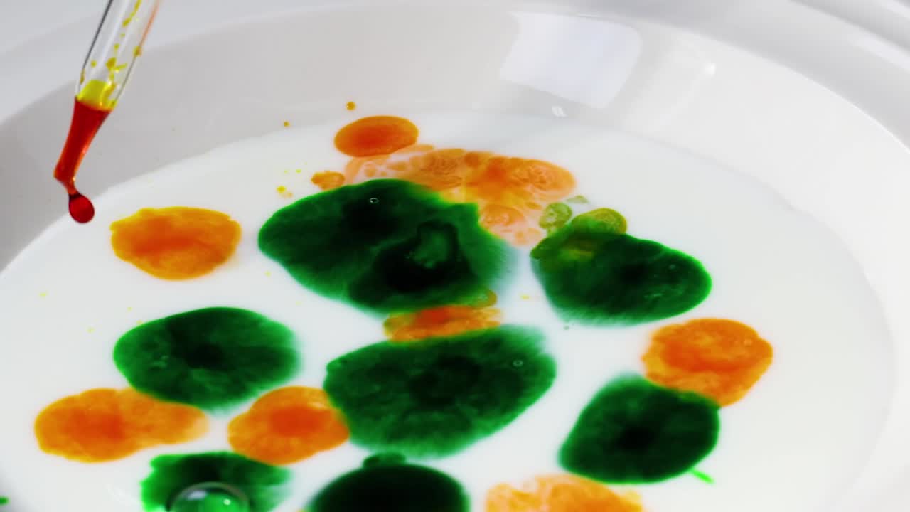 Watch vibrant green and orange dyes interact dynamically in milk using a pipette.