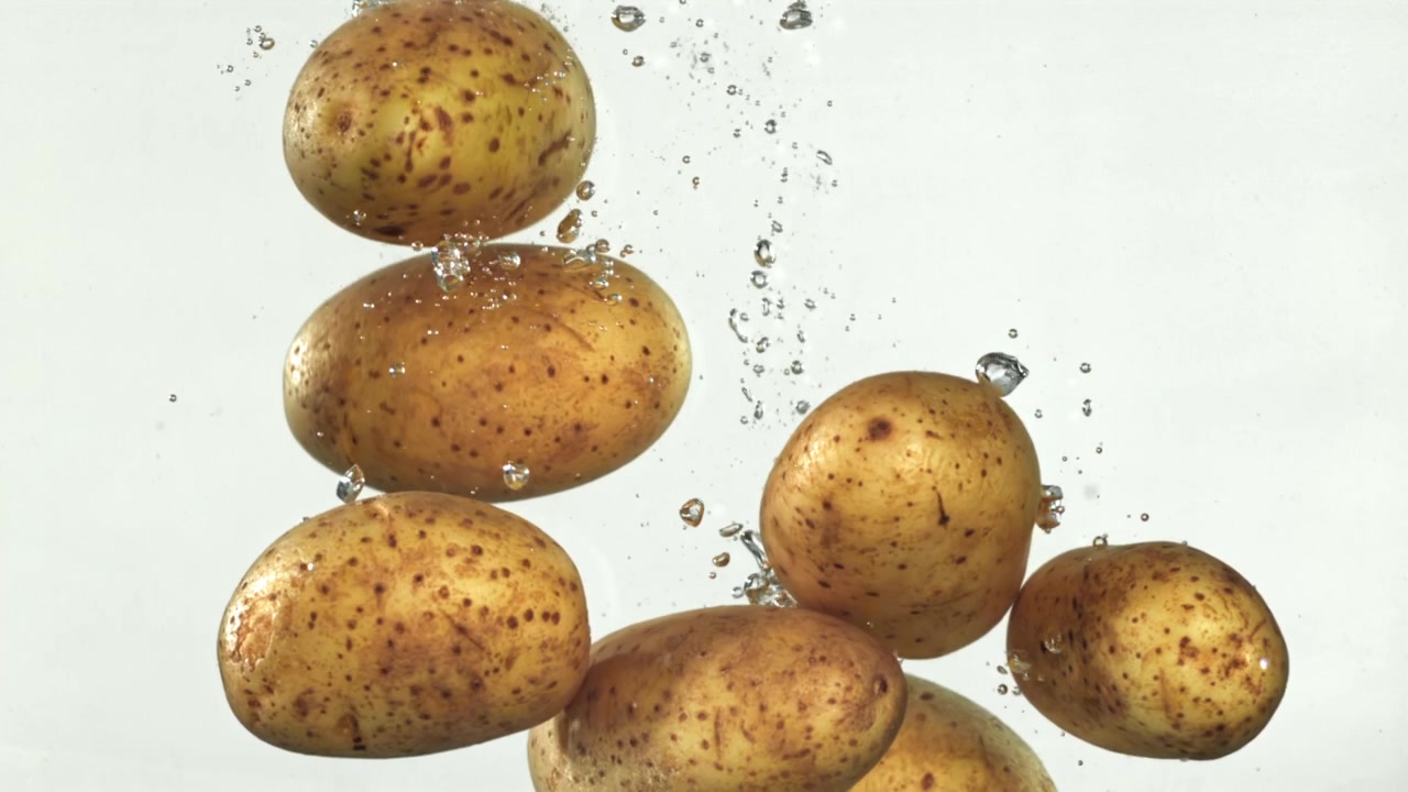 Patate fresche che cadono in acqua con bolle al rallentatore