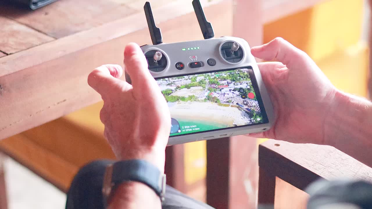 Hands operating a drone controller in Phuket, Thailand. Bright lighting highlights the screen displaying aerial footage