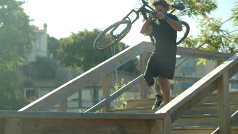 man with disability holding bike in hands and descending stairs