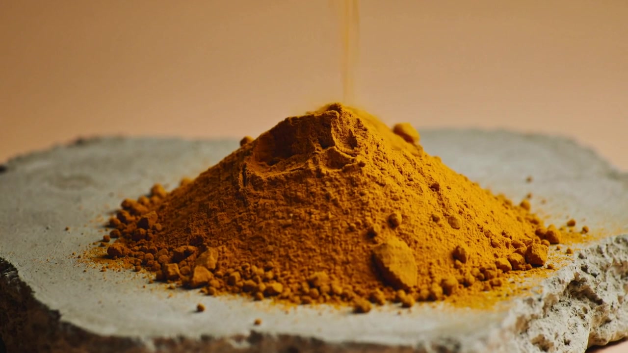 Pouring bright orange-yellow powder from above, conical mound forming on rough concrete slab