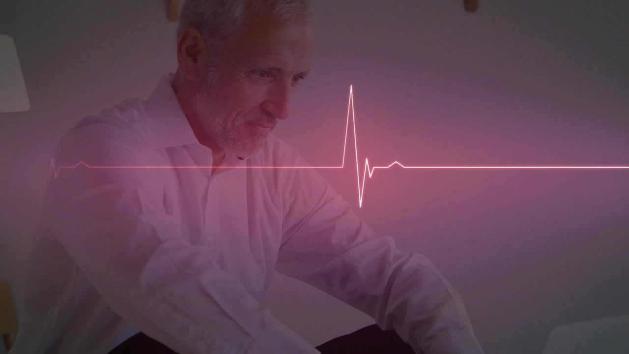 Mand sidder på sofa, læner sig mod tablet, tjekker hjertedata, mens lyserød EKG-linje bevæger sig.