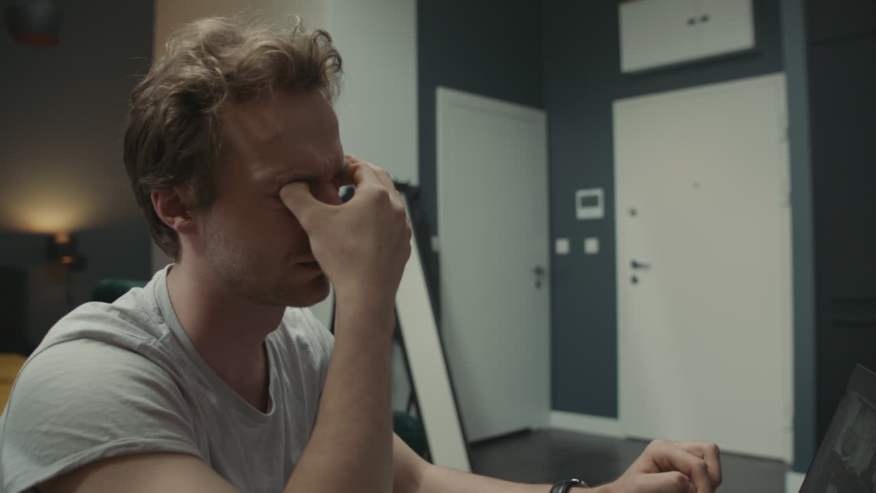 Man Working on Laptop at Home, Woman in Background