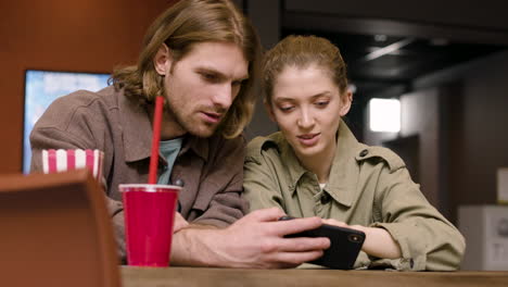 pareja feliz mirando algo divertido en el teléfono móvil en el cine