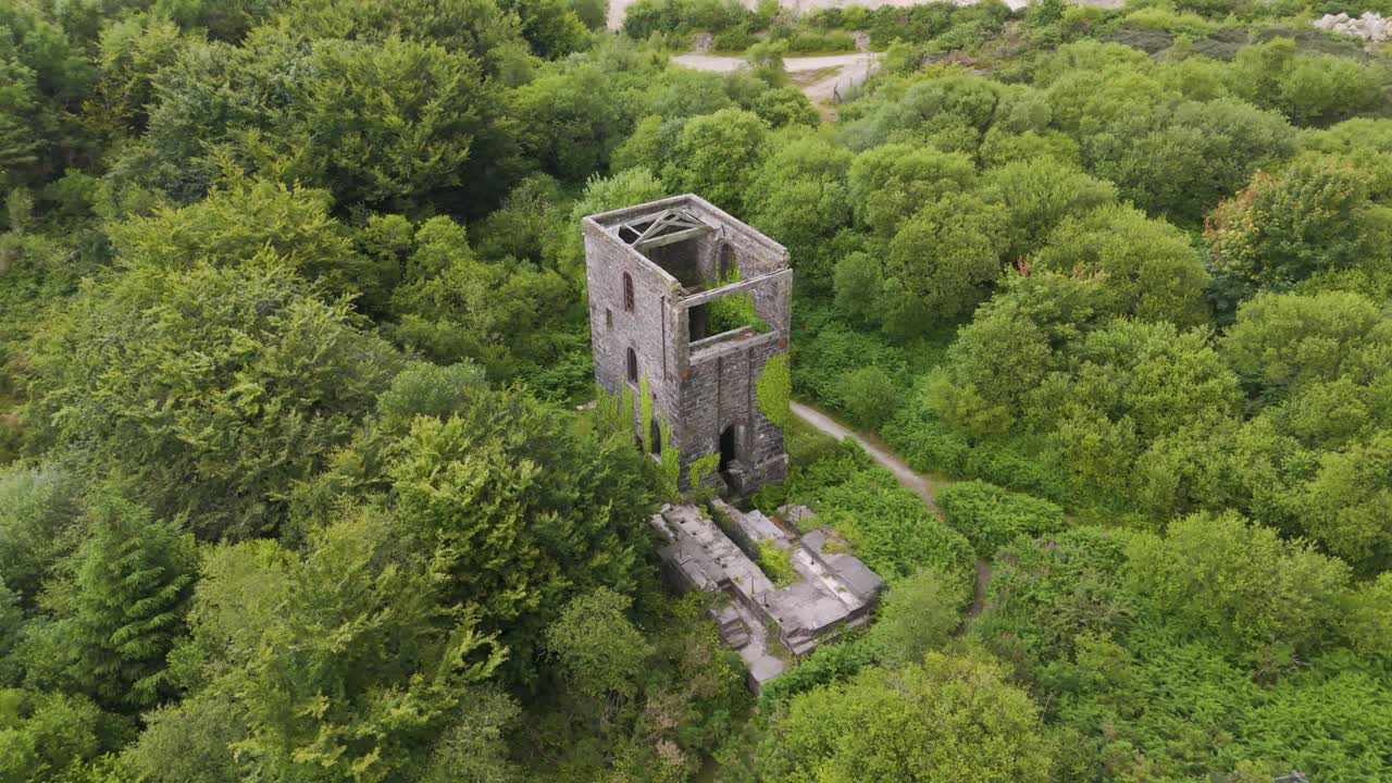Drone orbital view of a long-abandoned mine left to crumble with surrounding greenery, Cornwall, UK