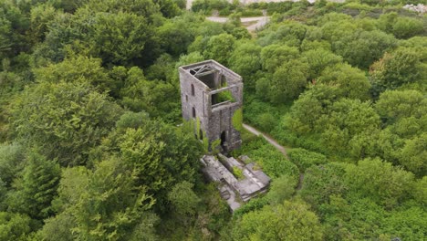drone orbital view of a long-abandoned mine left to crumble with surrounding greenery, cornwall, uk