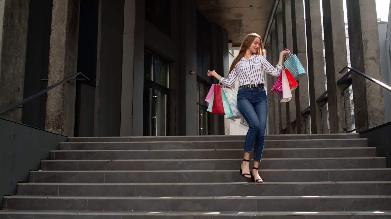 chica sonriente caminando desde el centro comercial con bolsas de compras, feliz con la compra en el viernes negro