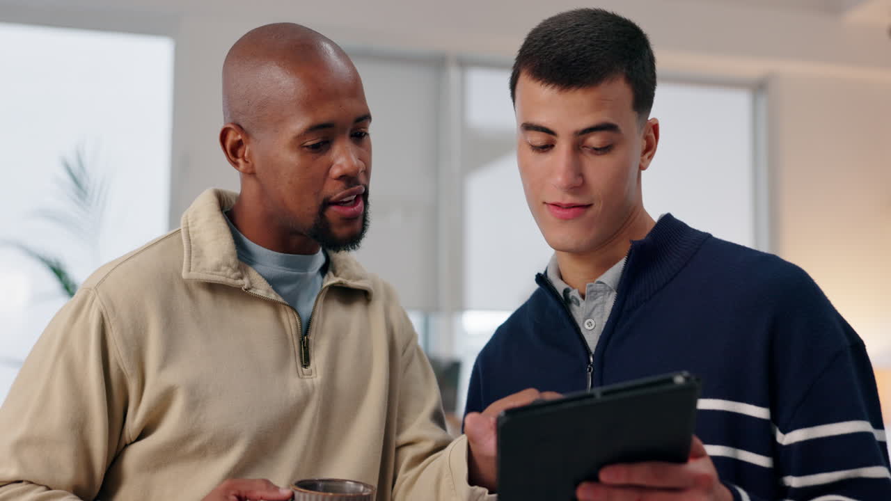 Two men looking at a tablet while having coffee
