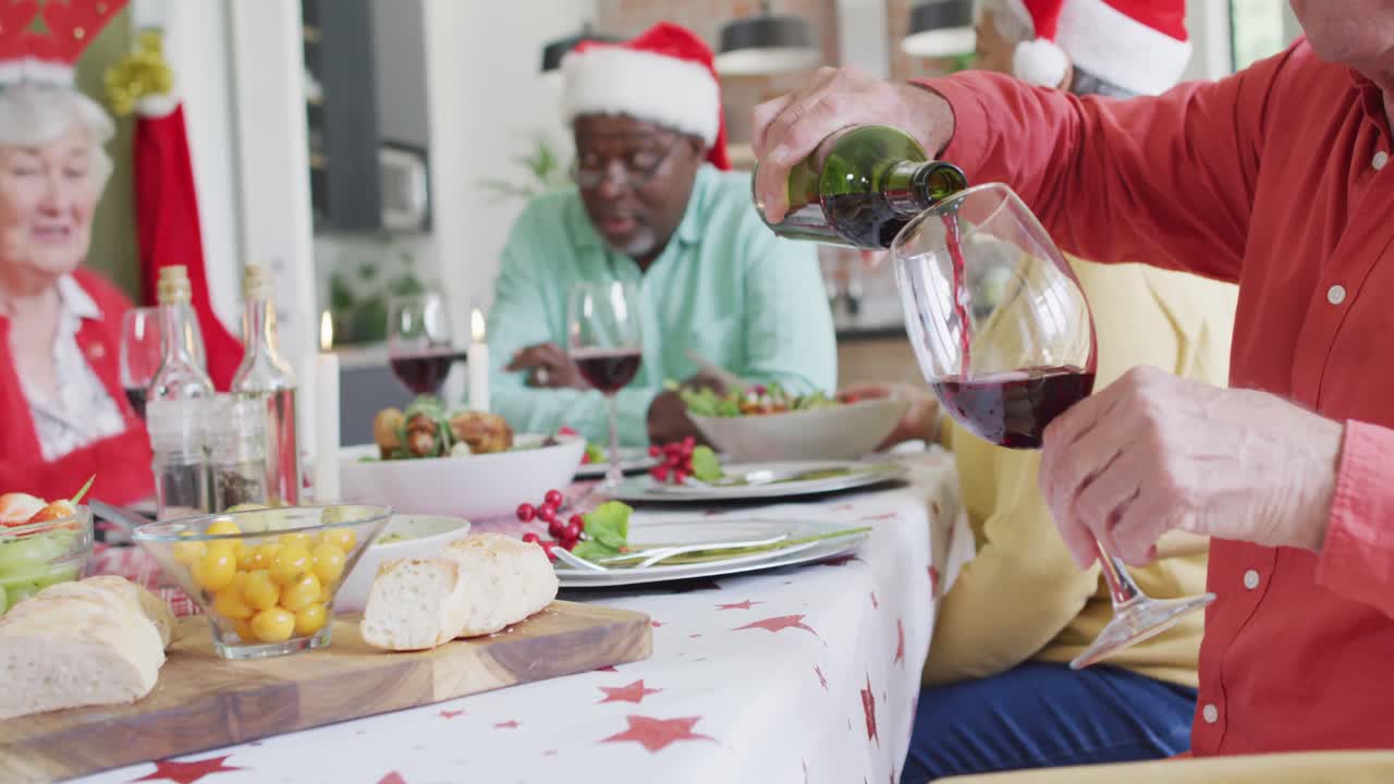 felices amigas y amigos mayores diversos celebrando la comida, vertiendo la vid en el tiempo de navidad