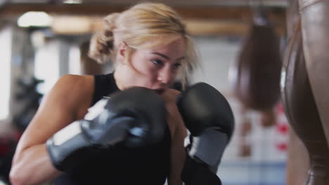 female boxer in gym training with old fashioned leather punch bag