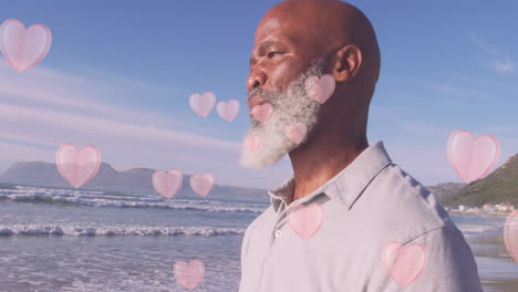 animation of hearts over senior african american man at beach