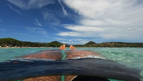 punto de vista de ángulo bajo en primera persona de las piernas y los pies del hombre relajándose mientras flota en el agua de mar en la playa de santa giulia en la isla de córcega, francia