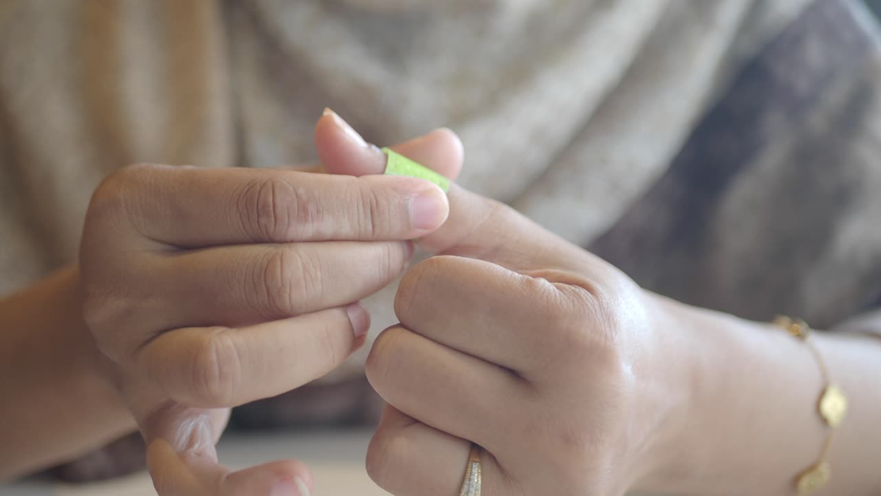 Close-up of hands applying a green bandage to a thumb
