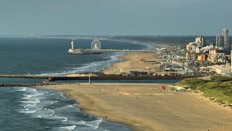 toma aérea de la hermosa playa de arena y la rueda de la fortuna en el muelle con la ciudad de den haag en el lado derecho