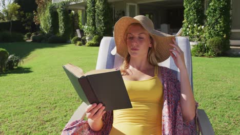 caucasian woman reading a book while sunbathing on a deck chair in the garden