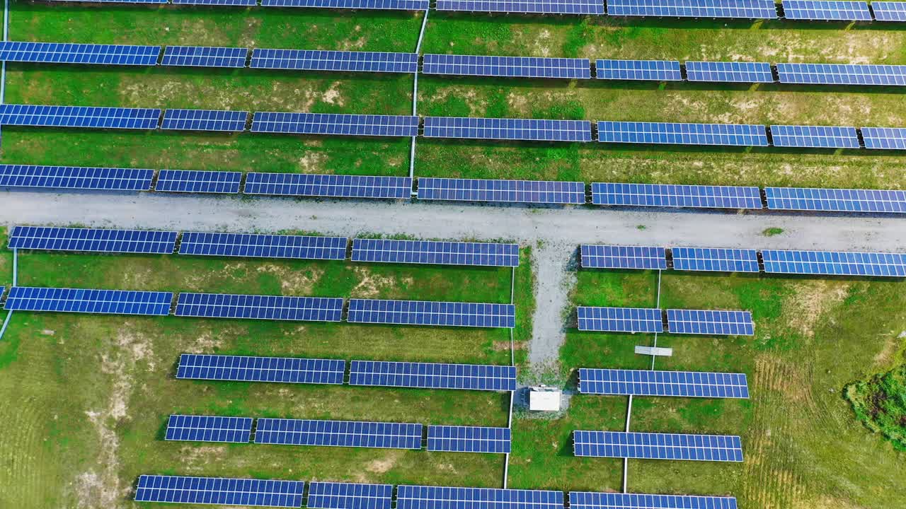 Modern solar station with blue panels standing in field with green grass under a bright sunlight. Green energy concept. Alternative power. Aerial view.
