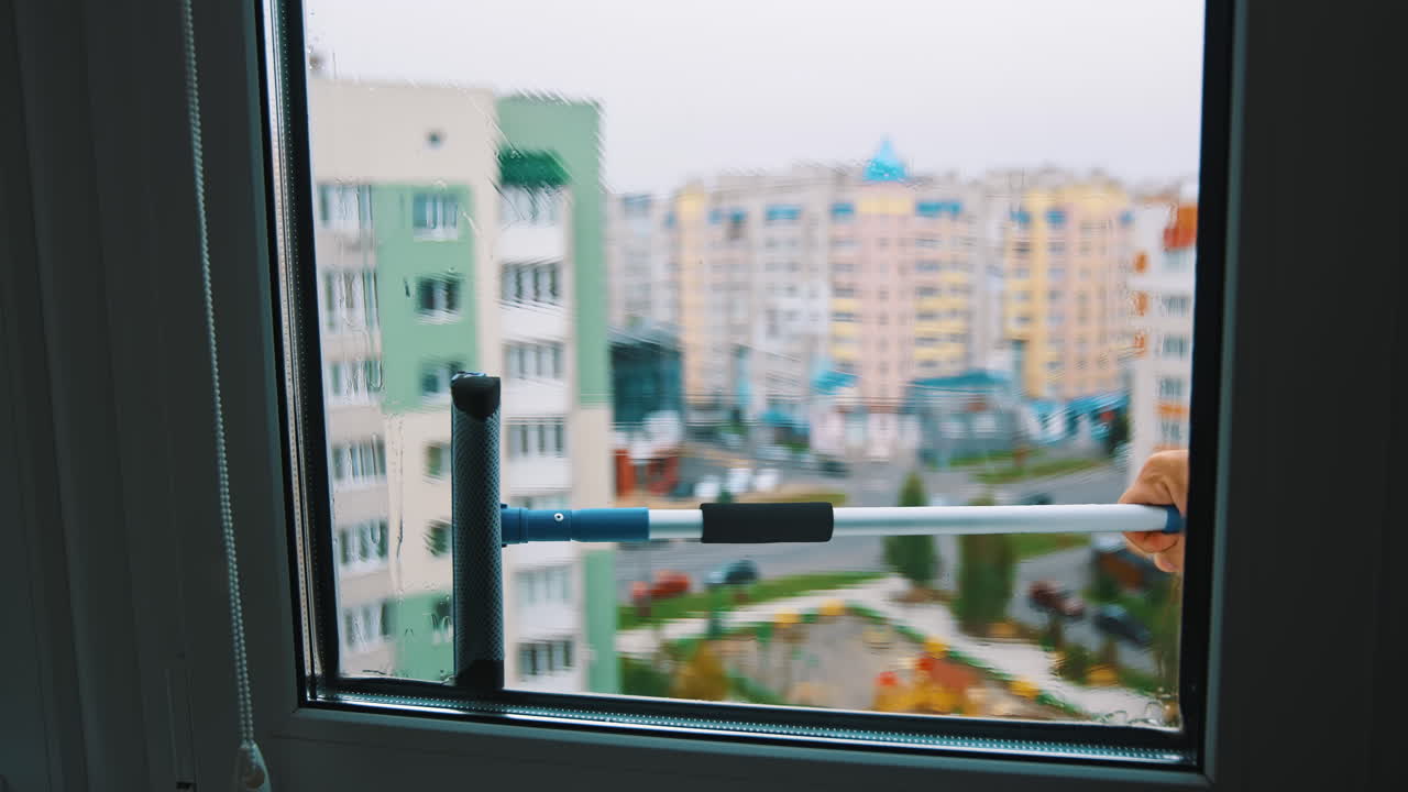 Brush washing window upstairs of a tall city building. Cleaning plastic window from outside on the urban background. View from indoors.