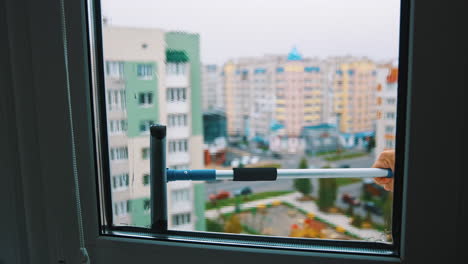 brush washing window upstairs of a tall city building. cleaning plastic window from outside on the urban background. view from indoors.