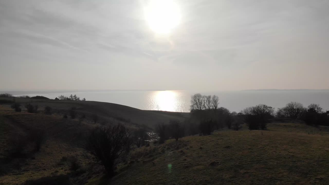 vista aérea de hermosas colinas verdes, moviéndose hacia la puesta de sol sobre el mar azul en sejerøbugten, dinamarca