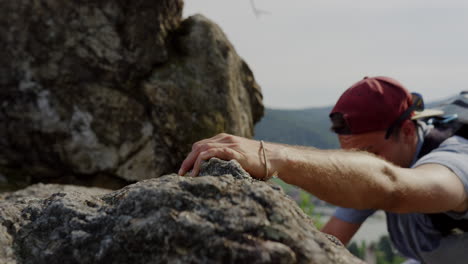 athletic-man-climbing-mountain,-close-up-hand-reaching-rocky-grip,-bouldering,-hazy-landscape-in-background,-fit-male-free-climb,-placing-hands-to-climbs-high,-altitude,-cinematic-shot,-slow-motion