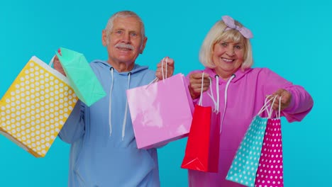 Senior-grandmother-grandfather-showing-shopping-bags,-advertising-price-discounts,-Black-Friday-sale