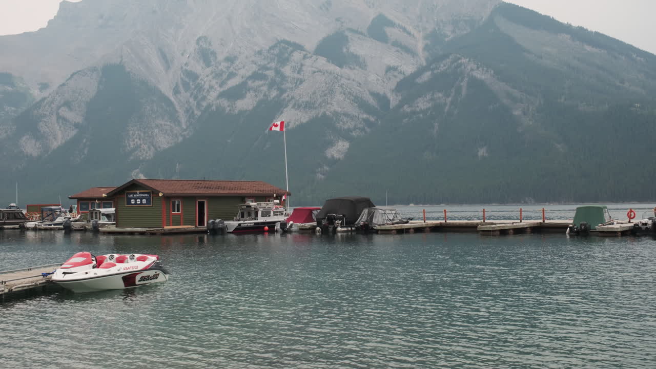The Canadian flag flutters over the Lake Minnewanka boathouse, with majestic mountains as a backdrop