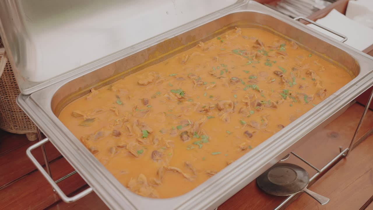 estofado de carne caliente en cremosa salsa naranja servido en una bandeja de buffet de acero inoxidable con hierbas frescas