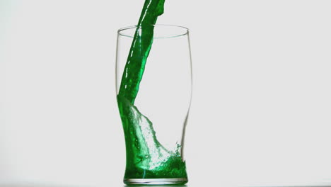 cerveza verde vertiendo en un vaso de pinta sobre un fondo blanco