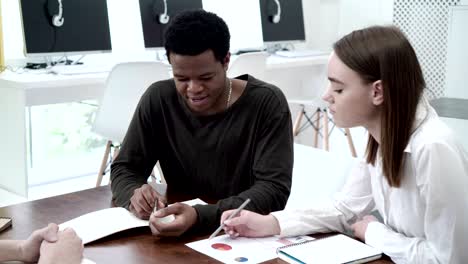 group of diverse economics students making project together. caucasian girl and african guy sharing ideas and taking notes at team meeting