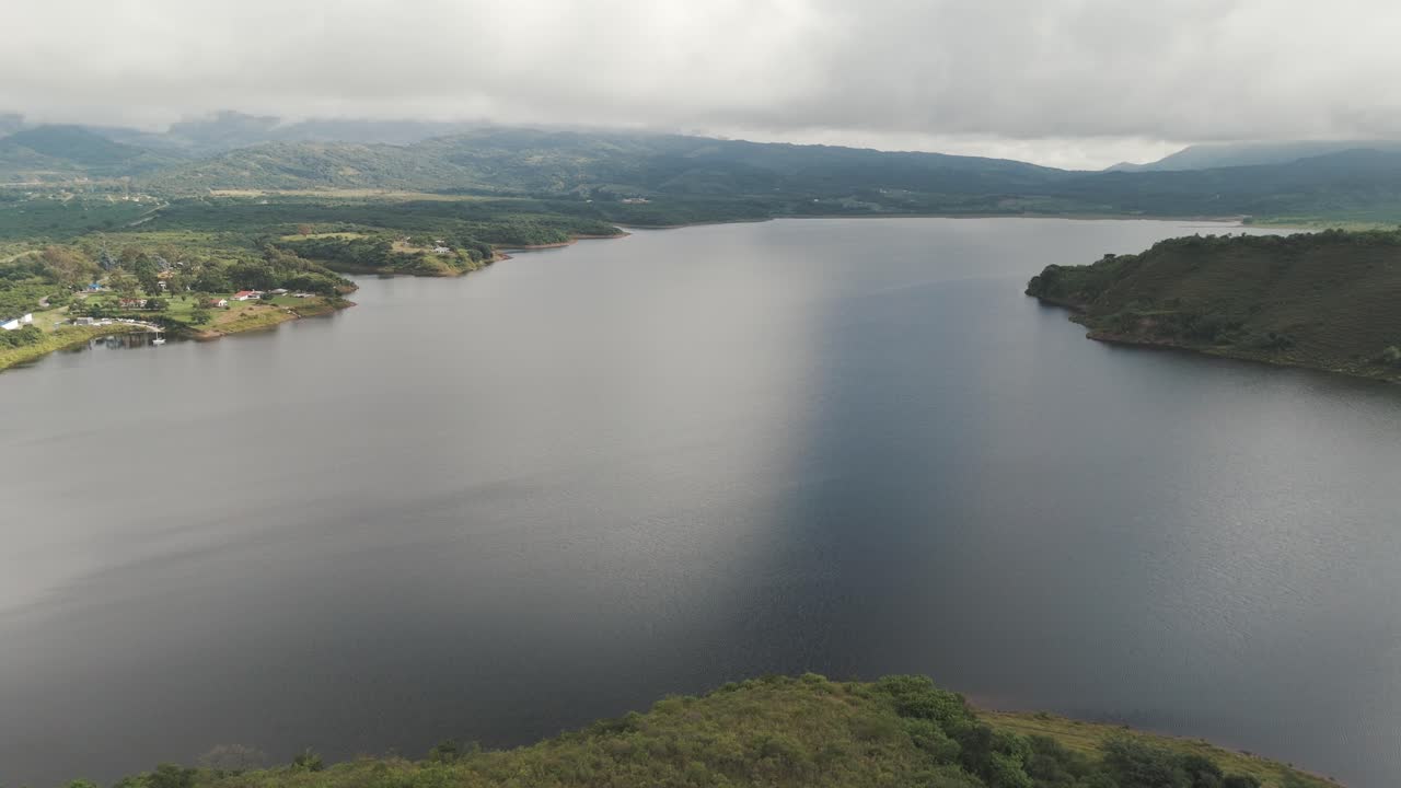 Aerial View of a Serene Lake Surrounded by Green Hills and Mountains under a Cloudy Sky