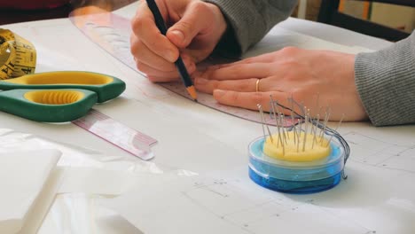el diseñador de moda está desarrollando el diseño de un nuevo vestido. la joven diseñadora de moda está dibujando un patrón de un nuevo modelo de vestido. primer plano de una mano de una joven diseñador de modas, ella está ocupada en cortar un nuevo modelo del vestido.