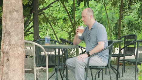 man sitting down drinking iced cappuccino coffee in the garden under a tree