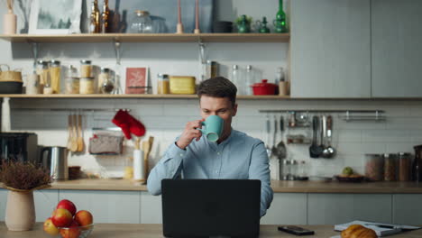 trabajador remoto bebiendo café trabajando en una computadora portátil desde casa. hombre sintiéndose relajado.