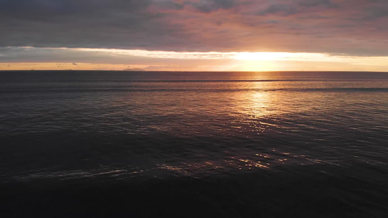수평선에 섬과 흐린 일출이 있는 해변과 잔잔한 바다 위로 옆으로 날아갑니다.