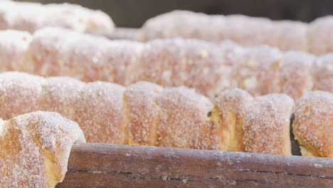 sugary spiral pastries rotate on a wooden rod, cooked over an open grill in bright natural daylight. close-up, shallow depth of field, steady camera