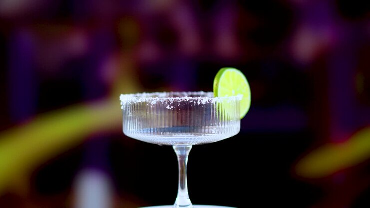 A margarita glass with a lime slice rotates against a vibrant background, showcasing its elegance and refreshing appeal