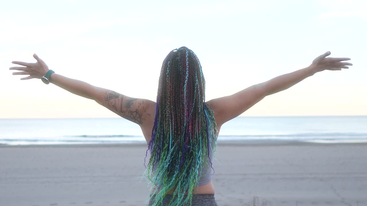 mujer con trenzas respira y extiende sus brazos en la playa