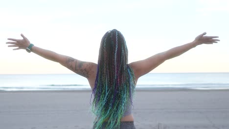 woman with braids breathes and spreads her arms on the beach