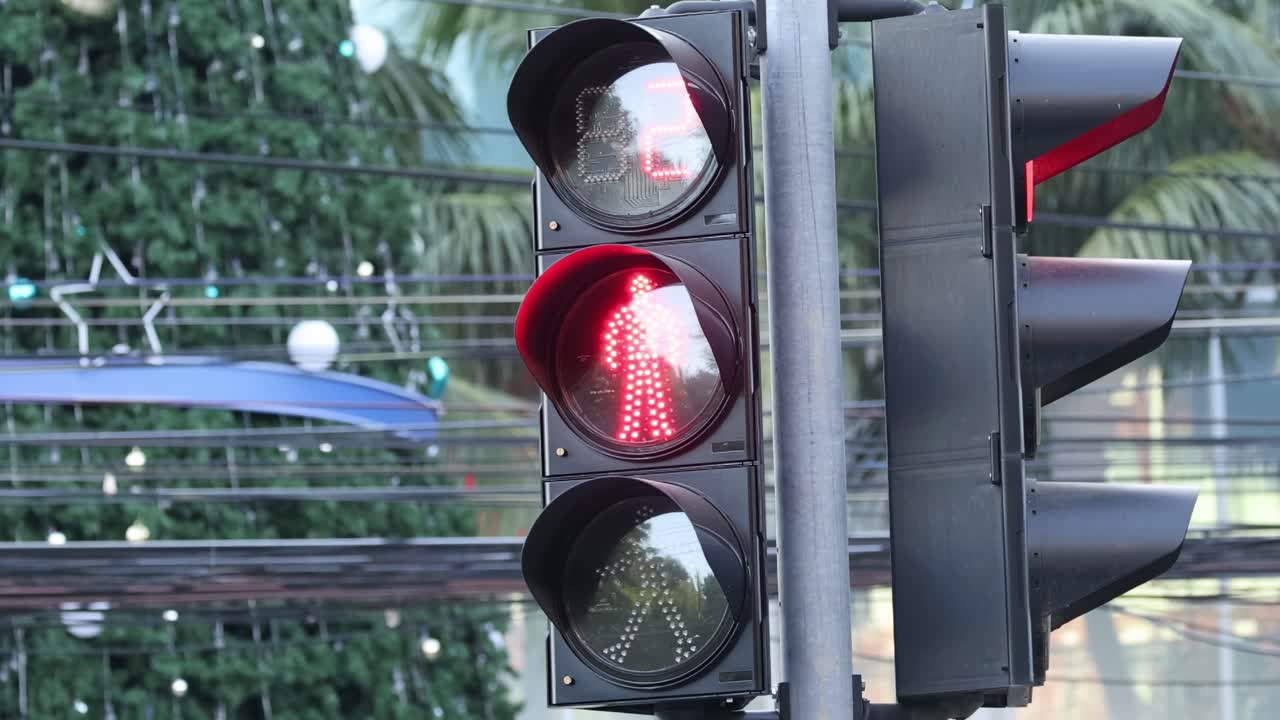 Close-up of a red traffic light against a backdrop of holiday decorations and palm trees.