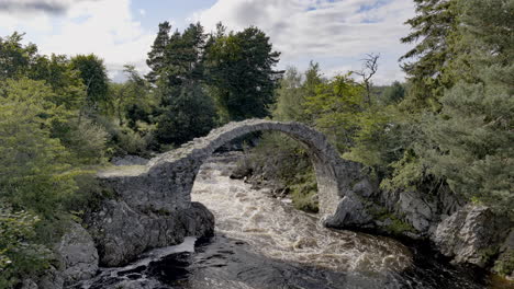 ruin of medieval ancient stone packhorse bridge over dulnain river, carrbridge, scotland, uk with strong water flow