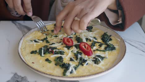 woman eating a spinach and cheese omelette with red pepper