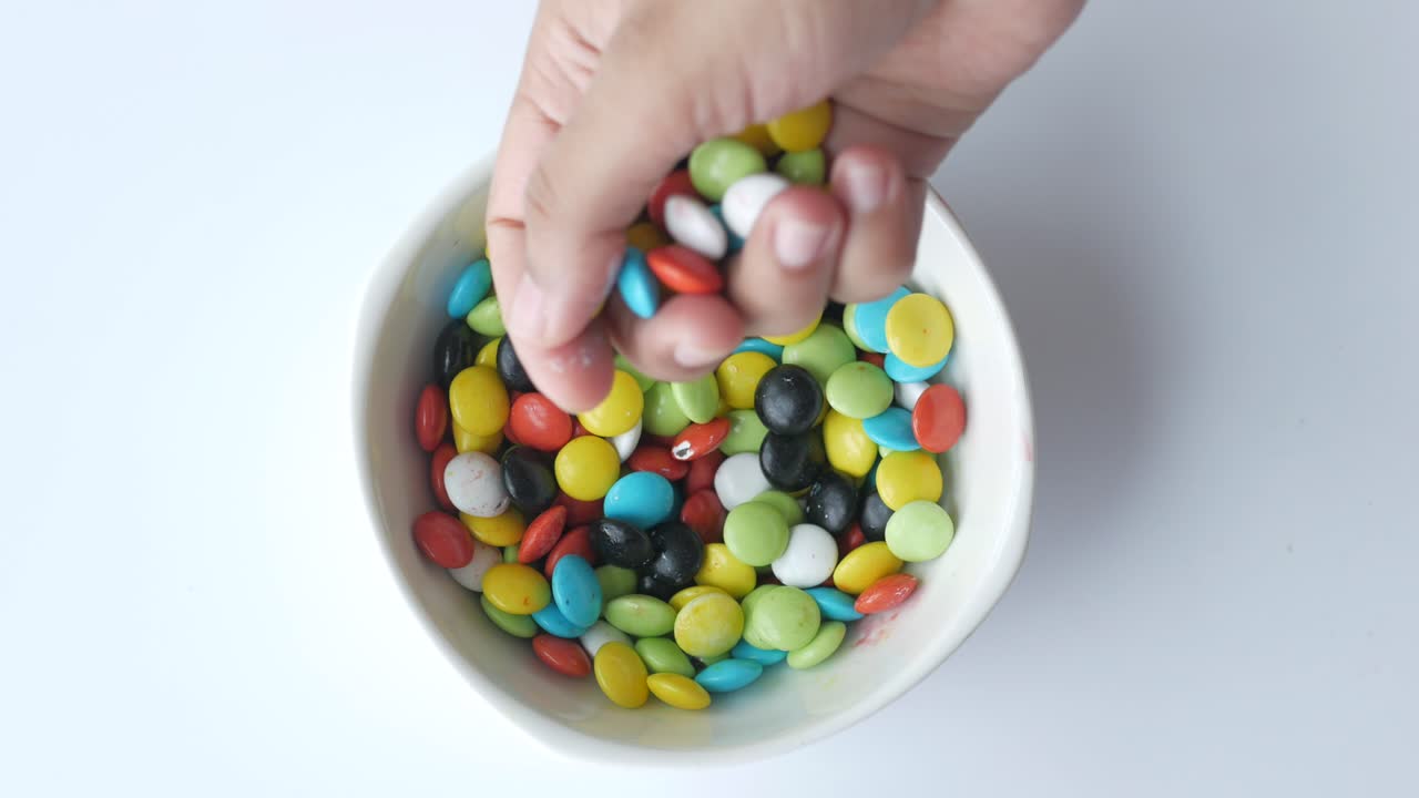 la mano vertiendo dulces de colores en un cuenco