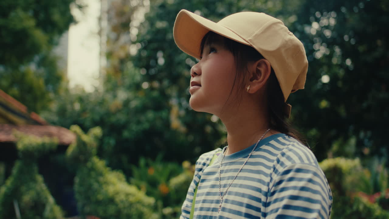 Young girl in striped shirt and cap, outdoors in nature, looking up with wonder