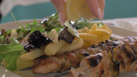 close up view of meal on the plate that woman waters lemon juice potatoes salad and chicken barbecue