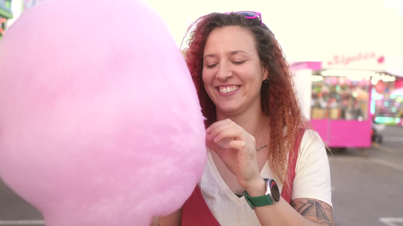 mujer feliz comiendo azúcar de algodón en la feria