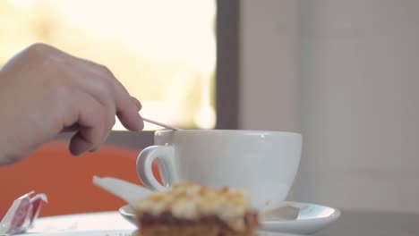 cena en la cafetería revolviendo una taza de café con pastel.