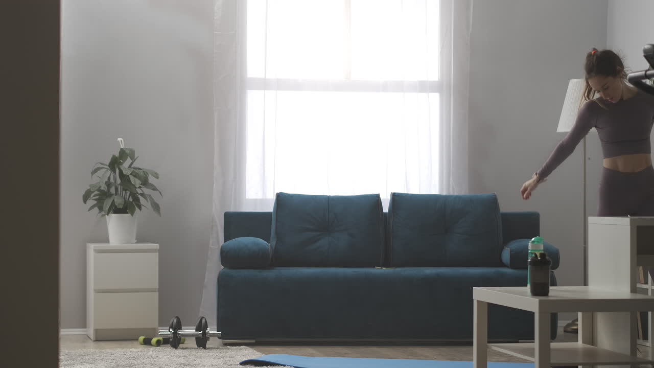 joven atlética con cola de caballo está tomando un descanso en casa entrenando relajándose y bebiendo agua caminando en la sala de estar de un apartamento moderno