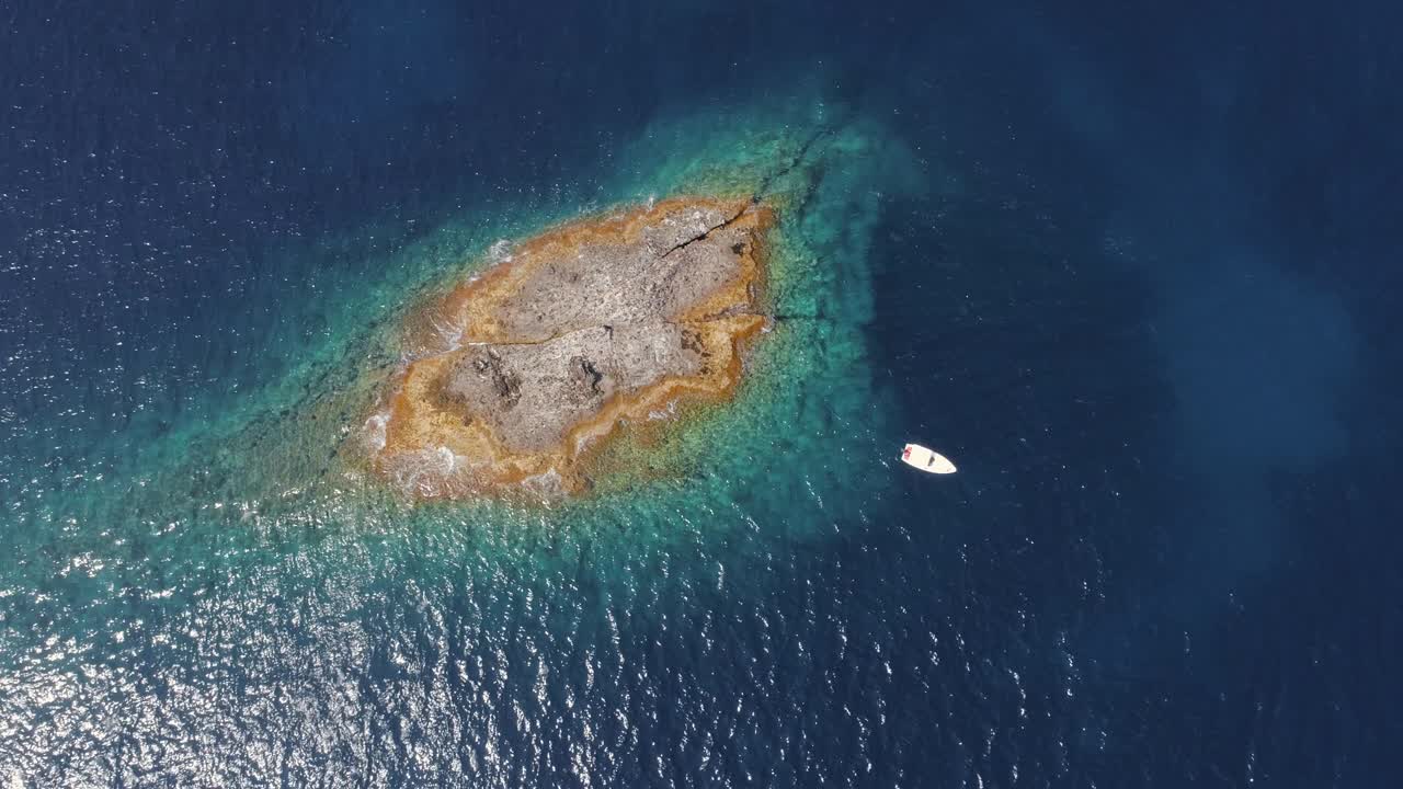 vista aérea superior pequeña isla de atolón con rocas y arena. agua azul clara y barco blanco desde un avión no tripulado.