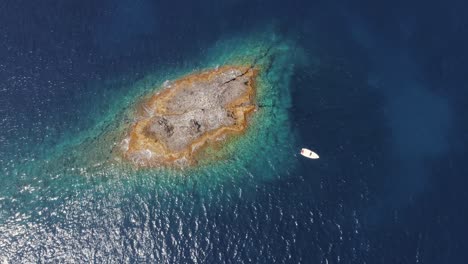 vista aérea superior pequeña isla de atolón con rocas y arena. agua azul clara y barco blanco desde un avión no tripulado.