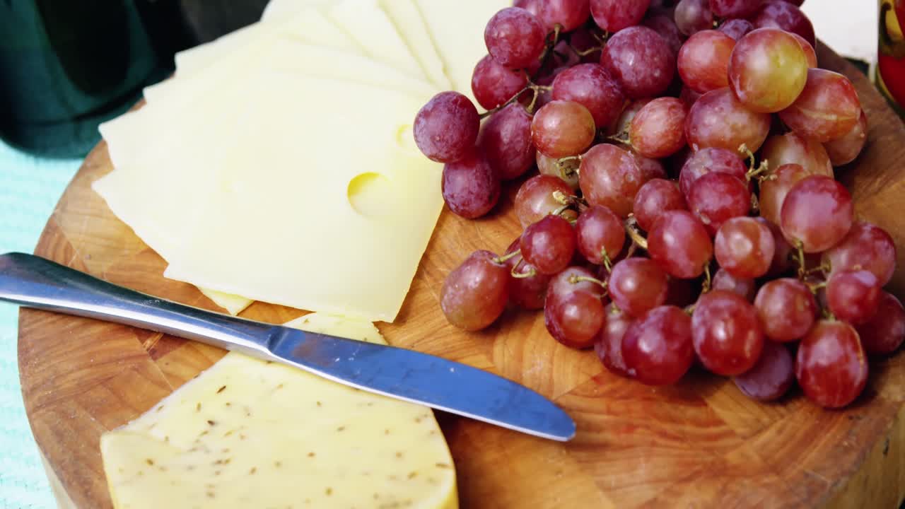 치즈 슬라이스, 빨간 포도 및 버터 칼을  ⁇ 는 보드에